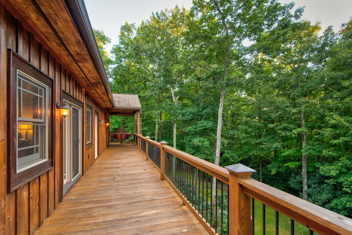A serene wooden deck with comfortable outdoor seating, bordered by leafy trees and lush greenery. The deck offers a tranquil space to unwind, enjoy scenic views, or spend time with family and pets.