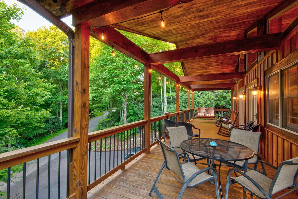 This deck scene is adorned with hanging lights, comfortable seating, and surrounded by rich greenery, capturing the essence of evening gatherings and the transition from day to night in a natural setting.