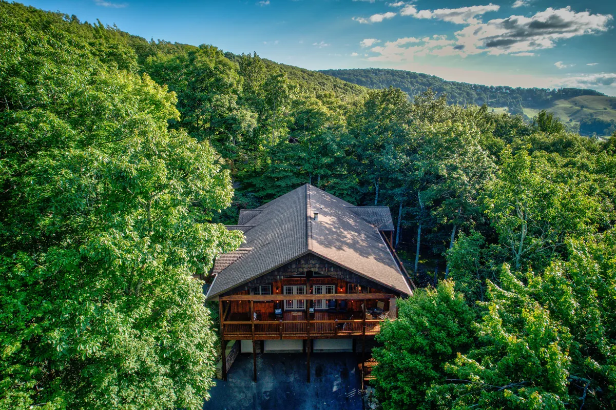 This image shows the wooden cabin nestled among lush trees with a stunning mountain backdrop, highlighting the tranquil, natural setting that surrounds the property. The scene evokes the allure of outdoor exploration and family gatherings in nature.
