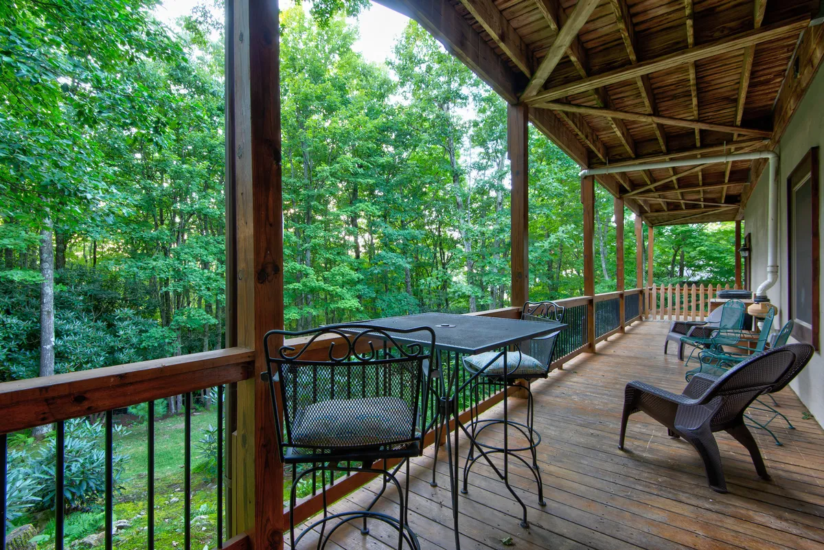 This image captures a wooden deck with bar stools and comfortable chairs, surrounded by lush trees. The vantage point suggests a serene, elevated space that directly connects guests to nature and the outdoors, perfect for viewing wildlife or enjoying mountain views at sunrise.