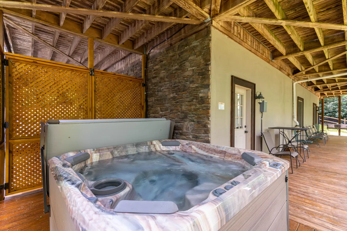 This image highlights a tranquil hot tub area framed by wooden beams and a stone wall, with outdoor seating set against a backdrop of nature. The space exudes relaxation and offers a rejuvenating amenity for guests of all ages.