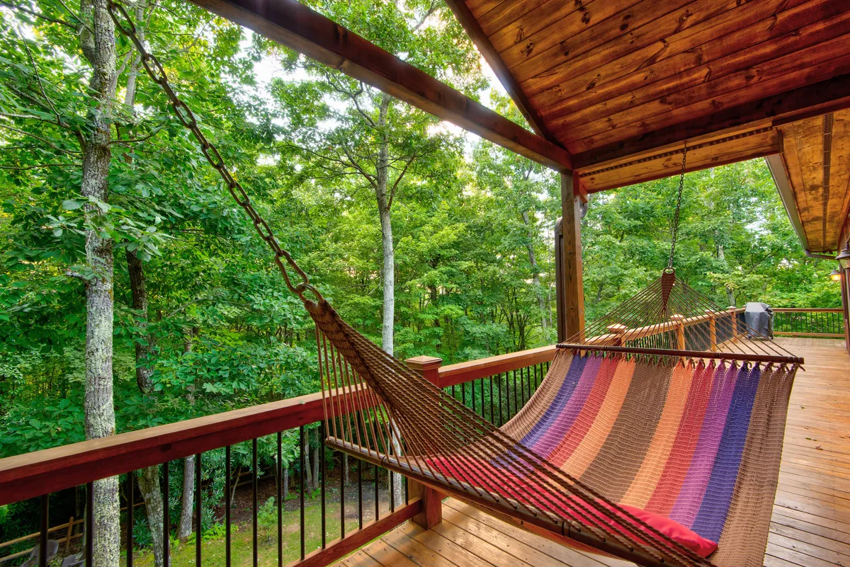 This image features a hammock strung across the wooden deck, bordered by lush greenery. Soft sunlight filters through the surrounding trees, creating a peaceful nook for relaxation. The tranquil setting encourages lounging, reading, or simply enjoying the fresh mountain air, all while being elevated above the forest floor.