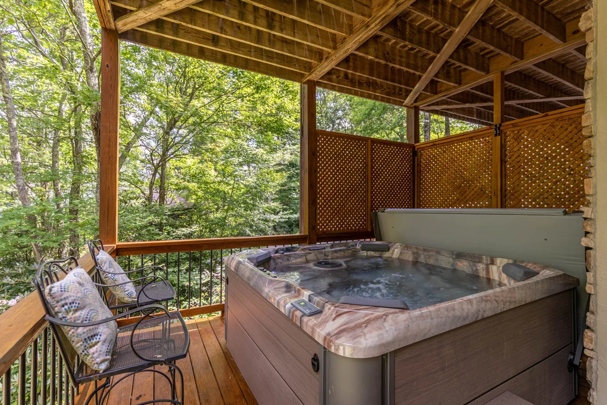 A tranquil outdoor scene featuring a private hot tub on a wooden deck, surrounded by trees. The deck provides a peaceful oasis for relaxation, socializing, or enjoying the sights and sounds of nature after a day of family activities.