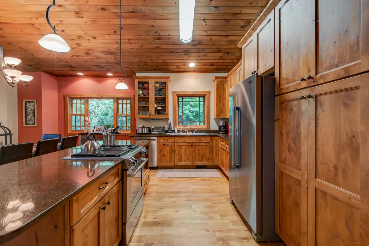 A beautifully appointed kitchen with a prominent island, stainless steel appliances, wood cabinetry, and generous windows letting in natural light. The setup encourages group meal prep and casual gatherings.