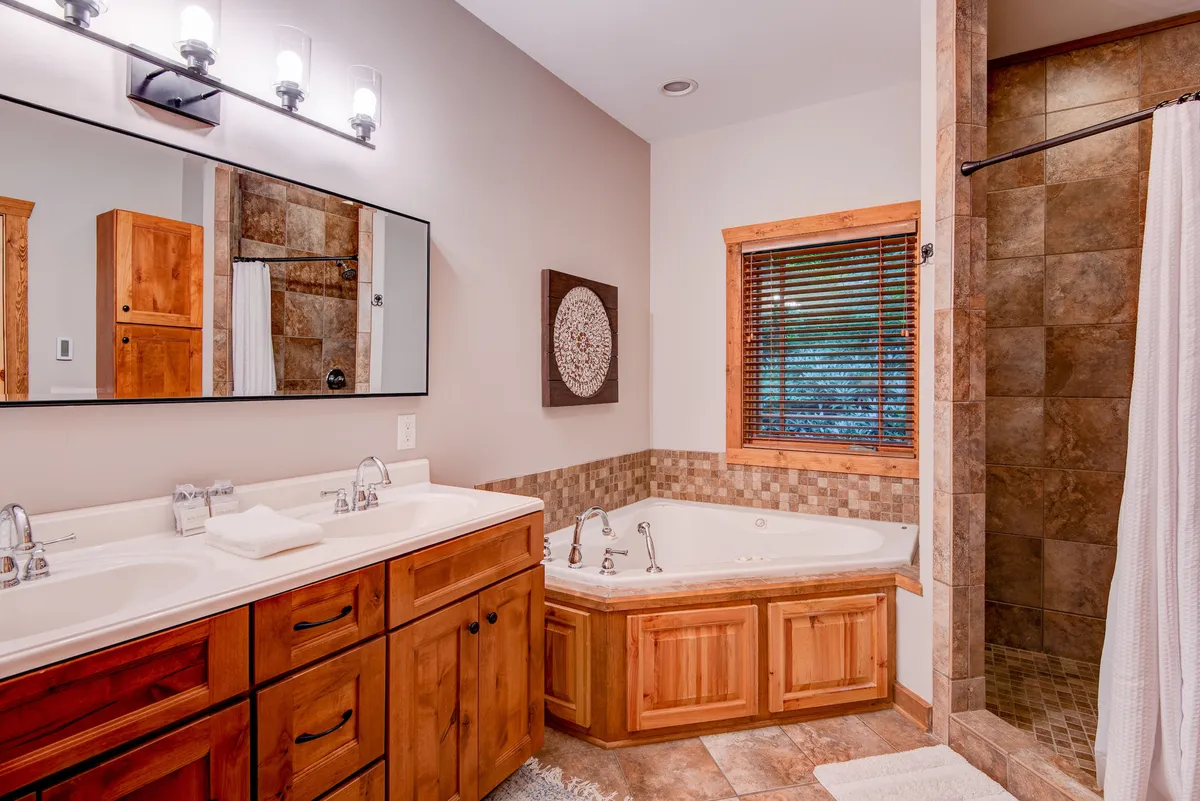 A serene, spa-inspired bathroom with dual vanity sinks, a luxurious jetted jacuzzi tub, a spacious shower area, wooden cabinetry, and elegant decorative wall art. The space feels both luxurious and functional, perfect for unwinding or preparing for the day.