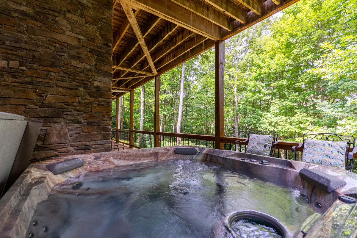 A bubbling hot tub sits on an outdoor deck, framed by sturdy wooden beams and panoramic natural views. Outdoor seating nearby encourages both group gatherings and solo relaxation, with the mountains and forested landscape setting the scene for rejuvenation after a day of adventure.
