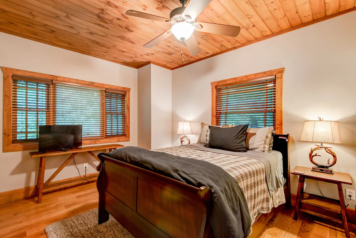 This interior photo features a tranquil bedroom with a comfortable bed, windows letting in abundant natural light, bedside lamps, and a television. The room exudes calmness with soft colors and tidy furnishings, making it an inviting and restful retreat.