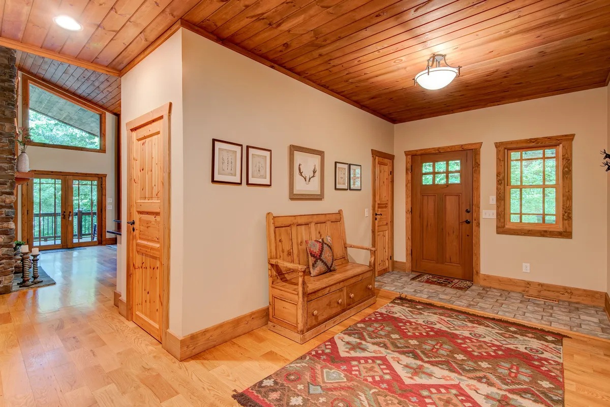 A welcoming foyer with a wooden bench, decorative rug, and framed artwork creates a homey first impression, viewed just inside the front door. The space is softly lit, highlighting the inviting, transitional area between the entry and the main communal living spaces.