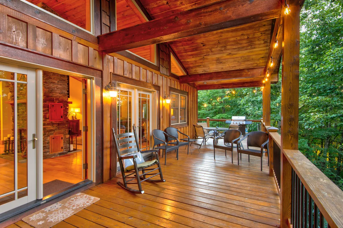 A cozy wooden deck featuring a rocking chair, outdoor seating, and lush greenery all around. The ambiance is welcoming, ideal for relaxing after an active day, and hints at evenings spent stargazing or gathering around a fire pit.