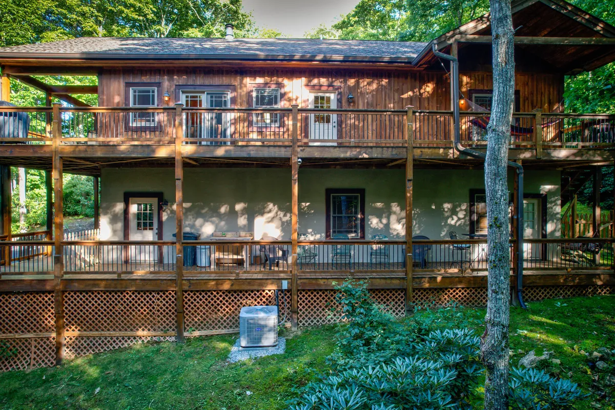 A wide wooden deck with seating, overlooking a backdrop of greenery and large windows from the cabin. The area looks out toward the woods, blending indoor comfort with outdoor access.