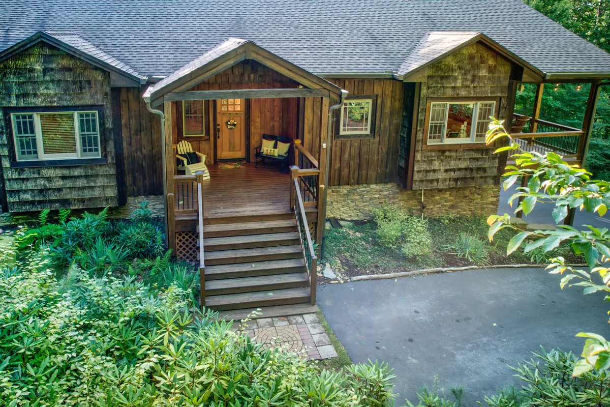The image displays a charming front porch with wooden steps, a welcoming doorway, and lush greenery surrounding the entrance. This space hints at a warm welcome for guests of all ages and a comfortable place to relax or wait for the group before an outing.